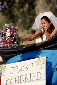 young bride with bouquet leaving reception with just married sign